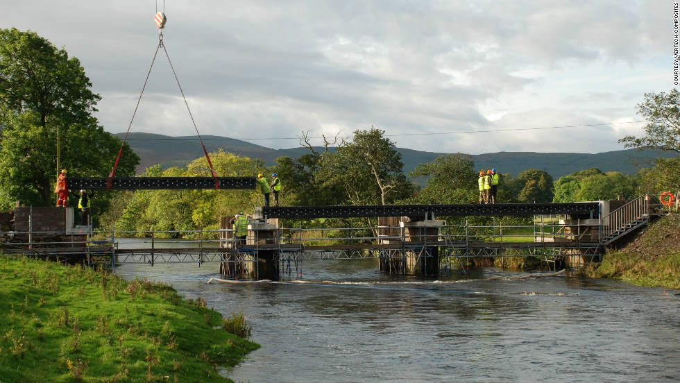 Third main beam of bridge made from recycled plastic is lowered into position by crane.